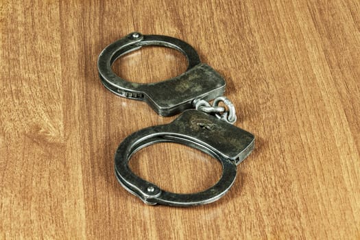 Metal handcuffs lie on a wooden table