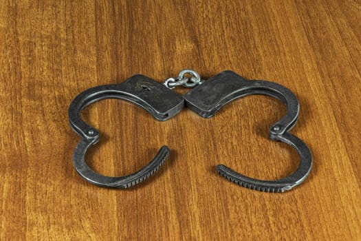 Metal handcuffs lie on the wooden surface