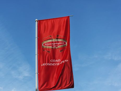 Red flag with the logo of the confectionery factory "Kommunarka" against the blue sky (Minsk, Belarus)