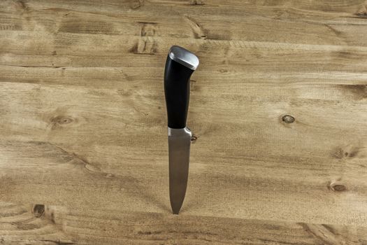 A metal knife with a black handle is stuck in a wooden stand