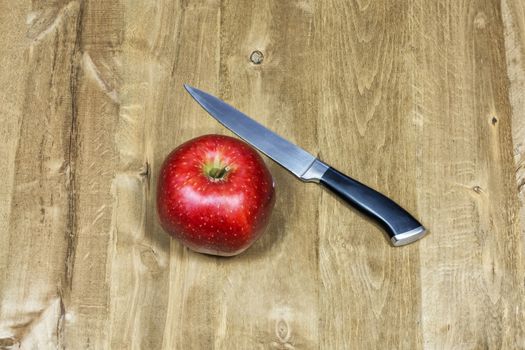 Knife and red apple lie on a wooden surface