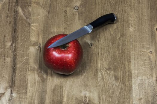 On the wooden surface are a red apple and a knife
