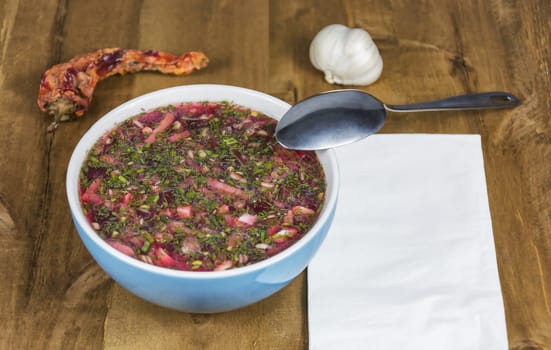 Red borscht in a blue porcelain bowl stands on a wooden table