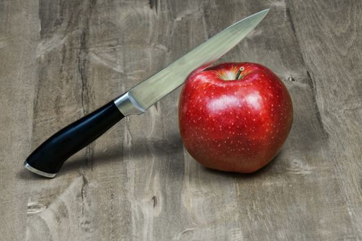 The knife cuts a red apple lying on a wooden surface