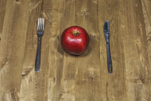 On the wooden surface lie a knife with a fork and a red apple