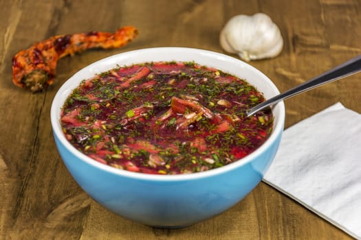 Red borscht in a blue porcelain bowl on a wooden table