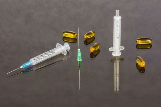 
On the glass surface there are two syringes, needles and capsules with medical preparations