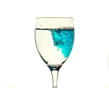 A glass glass with clear water is filled with a blue liquid