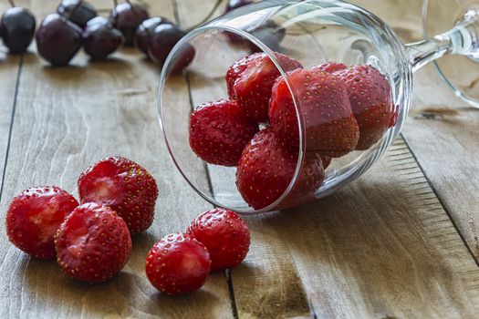 On a wooden table lies a glass wine glass with berries of strawberries and red apple