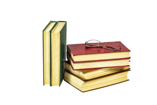 A pile of hard-bound books and reading glasses lie on a light background