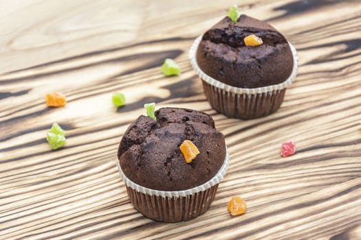 On a wooden surface a chocolate cake and candied fruit of different colors