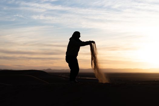 Silhouette of person jumping and throwing sand in the Sahara against a sunset. High quality photo