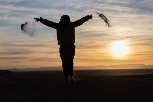 Silhouette of person jumping and throwing sand in the Sahara against a sunset. High quality photo