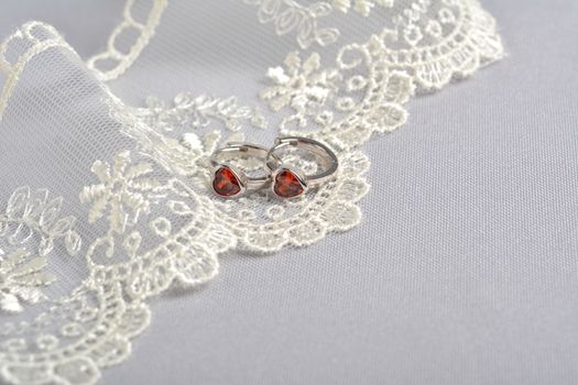 silver earrings with red glass hearts with delicate ecru lace on a light gray background. space for text. jewelry advertising texture