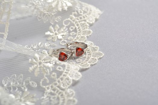silver earrings with red glass hearts with delicate ecru lace on a light gray background. space for text. jewelry advertising texture