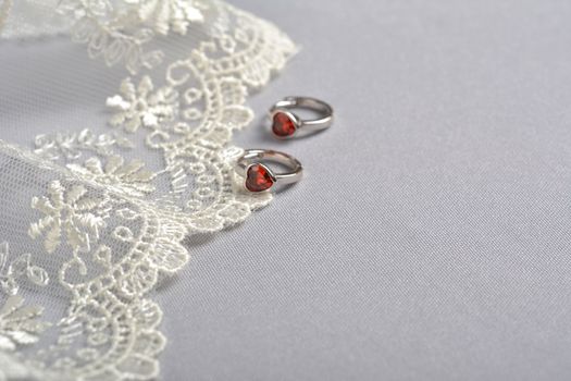 silver earrings with red glass hearts with delicate ecru lace on a light gray background. space for text. jewelry advertising texture