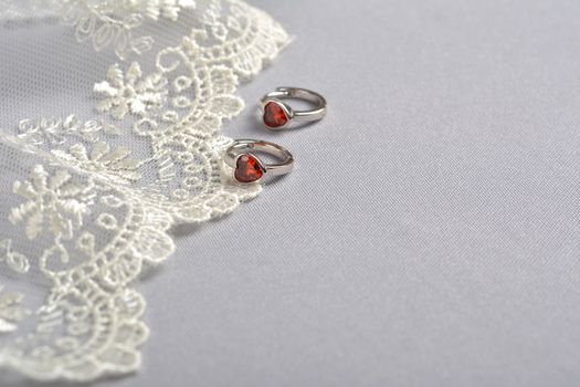 silver earrings with red glass hearts with delicate ecru lace on a light gray background. space for text. jewelry advertising texture