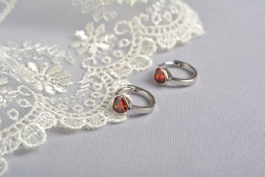 silver earrings with red glass hearts with delicate ecru lace on a light gray background. space for text. jewelry advertising texture