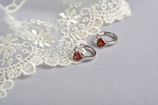 silver earrings with red glass hearts with delicate ecru lace on a light gray background. space for text. jewelry advertising texture