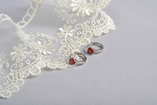 silver earrings with red glass hearts with delicate ecru lace on a light gray background. space for text. jewelry advertising texture