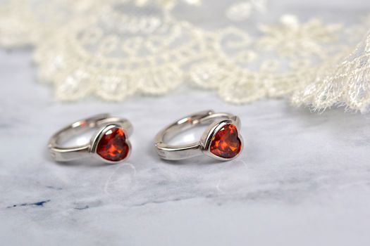 silver earrings with red glass hearts with delicate ecru lace on a light gray background. space for text. jewelry advertising texture