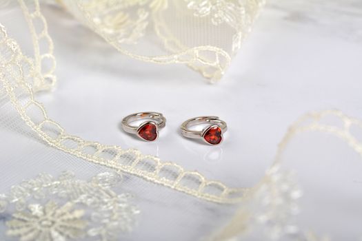 silver earrings with red glass hearts with delicate ecru lace on a light gray background. space for text. jewelry advertising texture