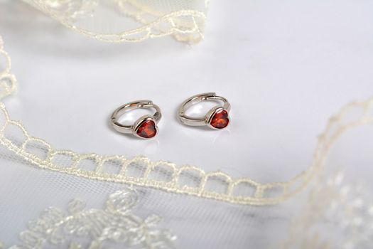 silver earrings with red glass hearts with delicate ecru lace on a light gray background. space for text. jewelry advertising texture