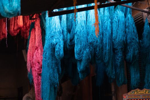 Dyed wool hanging to dry in souk in Marrakech Morocco Marrakechs Sebbaghine vibrant Dyers Souk. Skeins of red, blue, yellow, gold hanging from the ceiling with beautiful light shafting making a magical scene of ancient berber traditions High quality photo