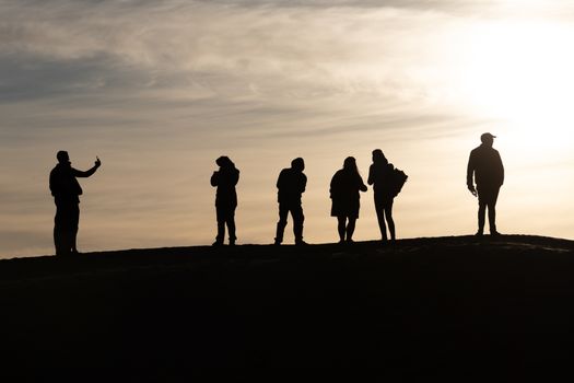 Silhouettes of tourists taking pictures at sunset in the Sahara desert Morocco. Set against a pale sky of blue and gold tourists on top of a sand dune. High quality photo