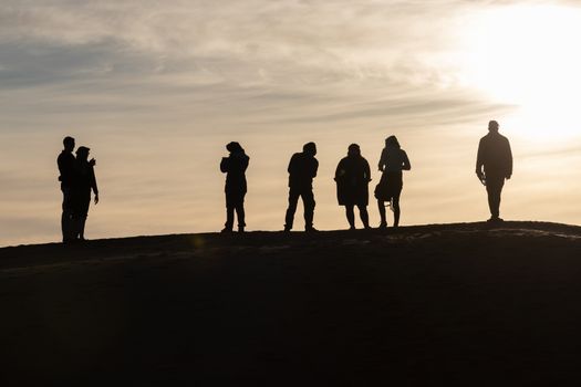 Silhouettes of tourists taking pictures at sunset in the Sahara desert Morocco. Set against a pale sky of blue and gold tourists on top of a sand dune. High quality photo