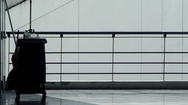 Silhouette image of cleaning service people sweeping floor with mop and other equipment on trolley.