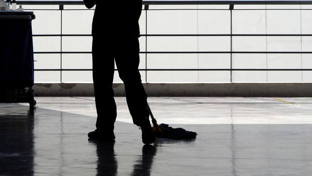 Silhouette image of cleaning service people sweeping floor with mop and other equipment on trolley.