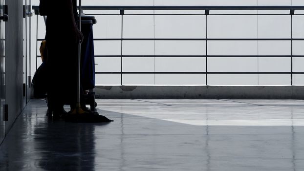 Silhouette image of cleaning service people sweeping floor with mop and other equipment on trolley.