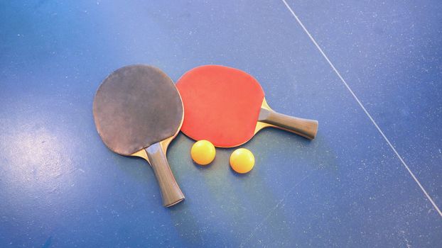 Top view of table tennis or ping-pong table with red and black color wood racket and yellow ball.