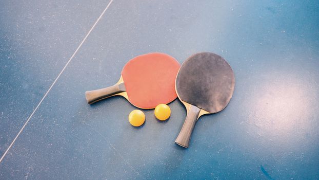 Top view of table tennis or ping-pong table with red and black color wood racket and yellow ball.