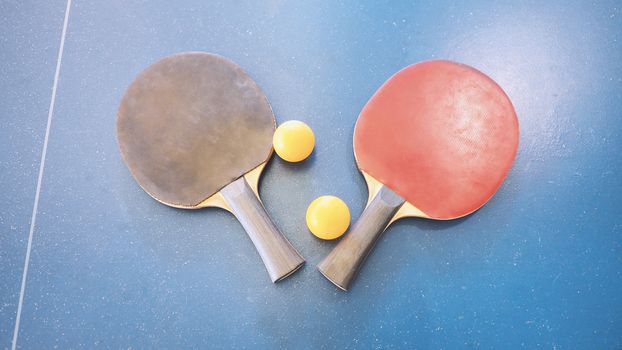 Top view of table tennis or ping-pong table with red and black color wood racket and yellow ball.