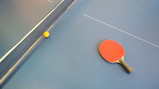 Top view of table tennis or ping-pong table with red and black color wood racket and yellow ball.