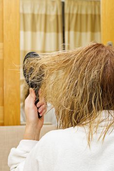 blond combing wet and tangled hair. Young woman combing her tangled hair after shower in hotel interior, close-up.