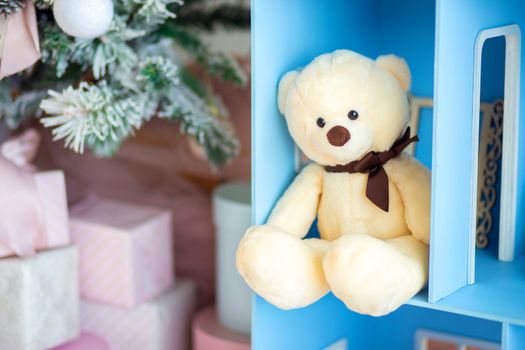 Cute teddy bear sitting in the dollhouse under the christmas tree. Gift for a child on New Year's Eve