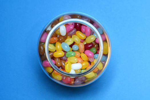 Top view of a glass jar filled with jelly beans on blue background