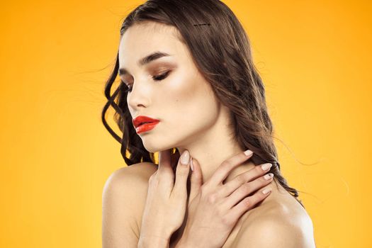 Beautiful brunette naked shoulders bright makeup red lips hairstyle close-up yellow background. High quality photo