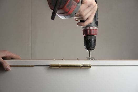 A worker twists a screw into the Board with a drill. The handyman does housework and improves the dwelling