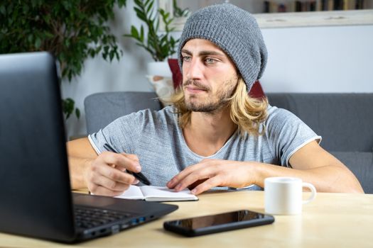 Handsome young caucasian man using computer working at home and learning online and writing notes