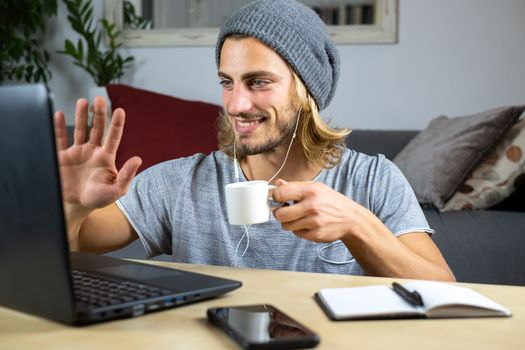 Handsome young caucasian man using computer working at home and talking with mobile feeling happy with smile showing teeth saying hello