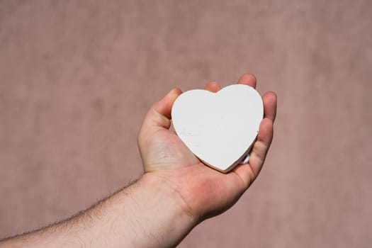 Hands holding a white wooden heart shaped object decoration isolated with copy space. Empty space template for your text.