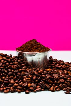 Coffee beans and portafilter with ground coffee in a composition on a pink background.