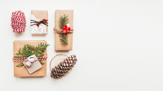 Christmas DIY presents wrapped in craft paper with fir tree twigs and red hearts. Top view on decorations on New Year gifts. Festive background. Winter holiday spirit. Banner with copy space.