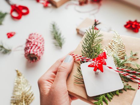 DIY presents wrapped in craft paper with fir tree twigs and red symbol of Christmas tree. Top view on decorations on New Year gifts. Festive background. Winter holiday spirit.