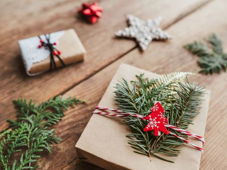 Christmas DIY presents wrapped in craft paper with fir tree twigs. Red decorations in shape of Christmas tree, stars. New Year gifts on wooden background. Winter holiday spirit.