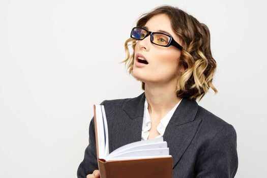 Woman at work with book in hand light background classic suit glasses head. High quality photo